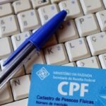 Caneta azul sobre teclado de computador com cartão CPF do Ministério da Fazenda